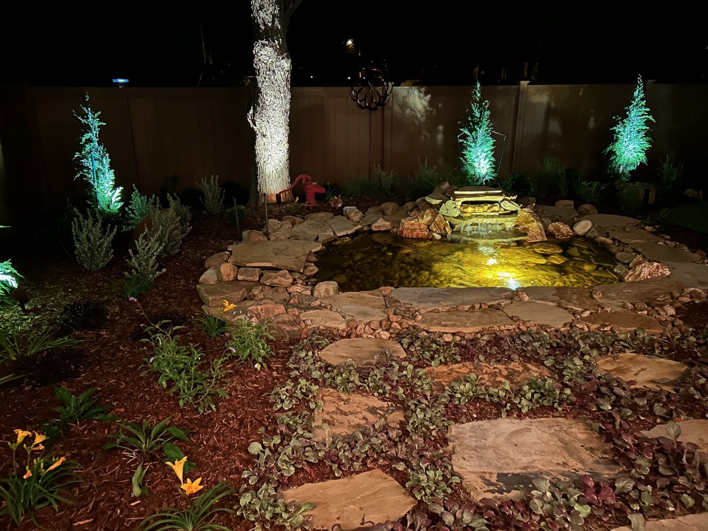 Backyard pond installed by Secret Gardens, lit in the evening